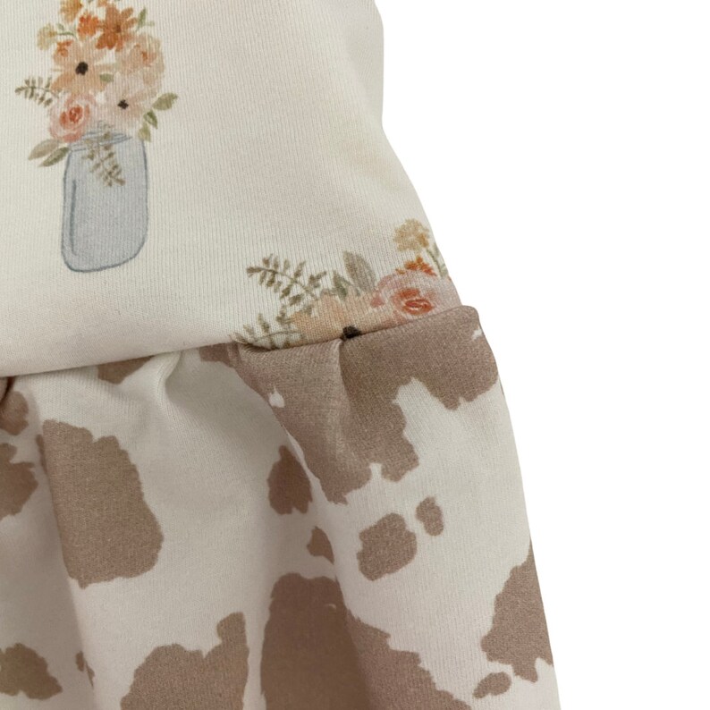 May include: A white fabric with a floral print and a cow print design. The floral print features a bouquet of flowers in a mason jar.