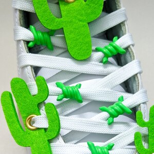 May include: White roller skate with green cactus-shaped charms on the laces and a green leather toe cap with a peacock feather eye design.