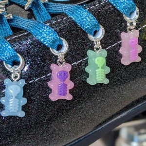 May include: Black roller skate with blue laces and colorful gummy bear charms. The charms are shaped like skeletons and are attached to the laces. The skate has a skull patch on the side.