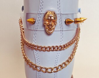 Puede incluir: Patín de ruedas blanco con cadenas doradas, un dije de calavera dorada y púas plateadas. Las ruedas son marrones con un patrón de mármol.