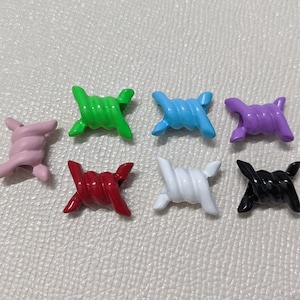 May include: Eight colourful barbed wire charms in various colours including green, blue, purple, pink, red, white, and black. The charms are made of metal and have a shiny finish.