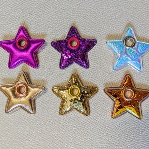 May include: Six star-shaped keychains with different colors and glitter finishes. Each keychain has a metal ring and a hole in the center.