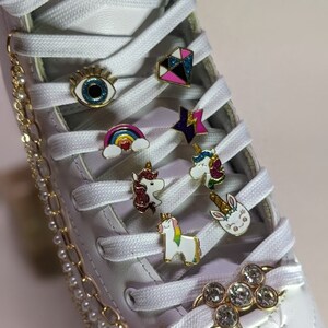 May include: White roller skate with decorative charms and a gold chain. Charms include a rainbow, unicorn, eye, star, and diamond. The chain has small pearls and connects to a rhinestone flower charm.