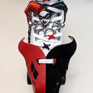 May include: White roller skate with a red and black leather toe cap. The toe cap has a diamond pattern on the red side and a heart on the black side. The skate has a Harley Quinn character patch on the laces.