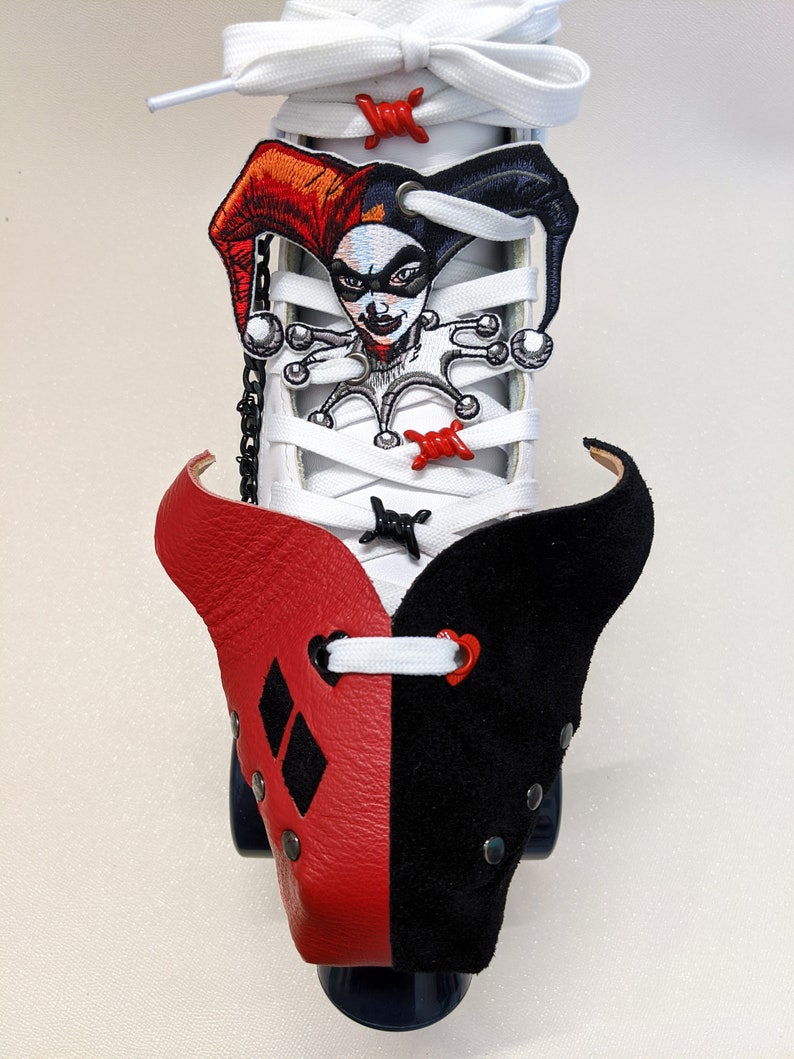 May include: White roller skate with a red and black leather toe cap. The toe cap has a diamond pattern on the red side and a heart on the black side. The skate has a Harley Quinn character patch on the laces.