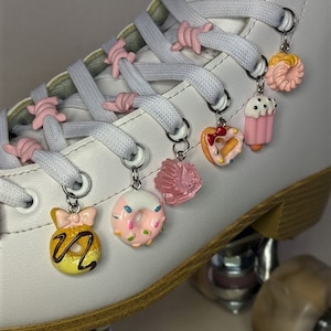 Puede incluir: Patín blanco con abalorios de zapatos en forma de donut rosa y amarillo. Los abalorios están unidos a los cordones del patín.