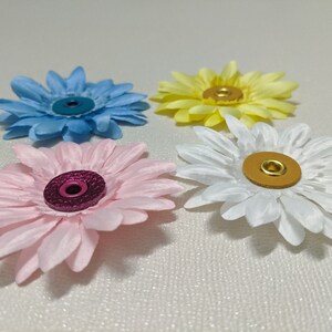 May include: Four fabric flowers with different colored centers. The flowers are light blue, pink, white, and yellow. Each flower has a metal button in the center.