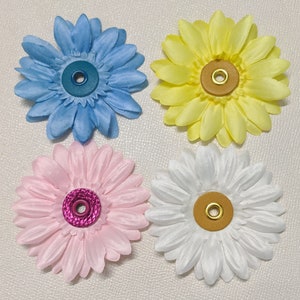 May include: Four fabric flower embellishments with a button center. The flowers are in shades of blue, yellow, pink, and white.