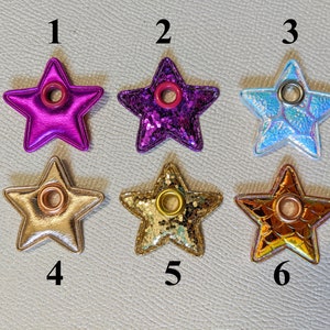 May include: Six star-shaped fabric embellishments with a hole in the center. The stars are in various colors and textures, including purple, gold, and iridescent.