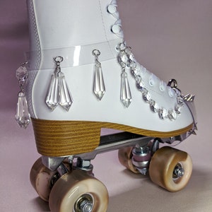 May include: White roller skate with a wooden platform and clear crystal embellishments. The skate has a white leather boot with a lace-up closure and a clear plastic strap with crystal dangles.