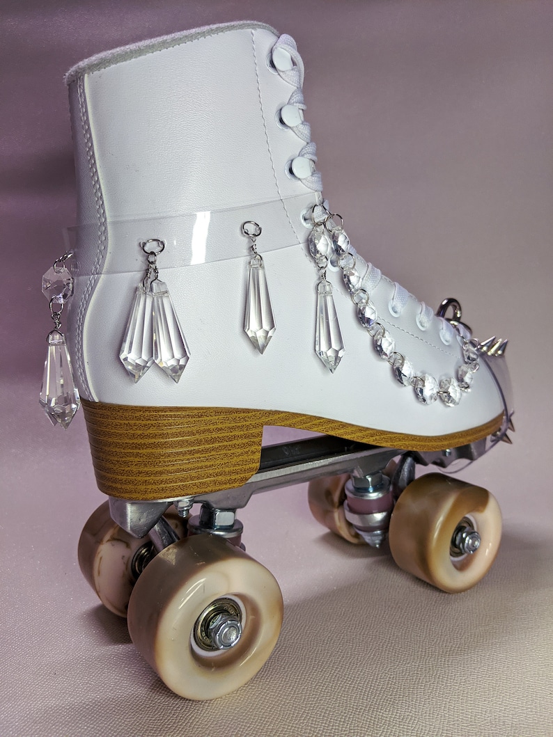 May include: White roller skate with a wooden platform and clear crystal embellishments. The skate has a white leather boot with a lace-up closure and a clear plastic strap with crystal dangles.