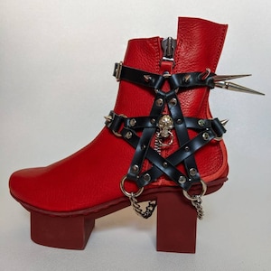 May include: Red leather ankle boot with a black pentagram strap and a skull charm. The boot has a thick platform sole and a zip on the side.