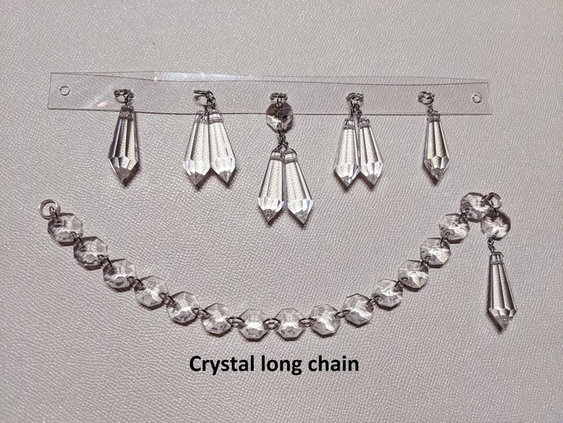 May include: A crystal long chain with multiple crystal drops hanging from a clear plastic strip. The chain is made of faceted crystal beads and has a single crystal drop hanging from the end. The text "Crystal long chain" is printed below the chain.