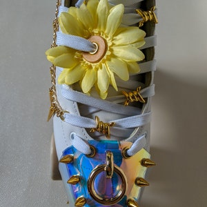May include: White roller skate with gold chain, barbed wire, and a yellow flower on the laces. The toe stop is a gold ring with spikes.
