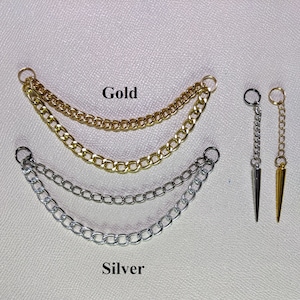 Peut inclure: Bijoux de cha&icirc;ne dor&eacute;s et argent&eacute;s. L'image pr&eacute;sente deux ensembles de bijoux de cha&icirc;ne, l'un dor&eacute; et l'autre argent&eacute;. Chaque ensemble comporte deux cha&icirc;nes. L'image montre &eacute;galement deux boucles d'oreilles &agrave; cha&icirc;ne unique avec un pendentif en forme de pointe, une dor&eacute;e et une argent&eacute;e.