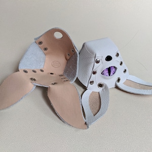 May include: White leather bunny mask with purple eye detail and silver rivets. The mask is open, revealing the interior construction and a "HAND MADE" stamp. The mask has long ears and is designed to be worn.