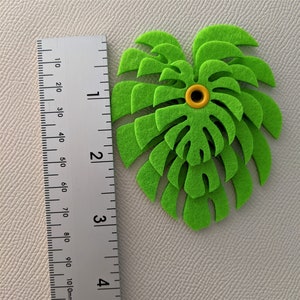 May include: A green felt monstera leaf cutout with a yellow button in the center. The leaf is approximately 3 inches wide.