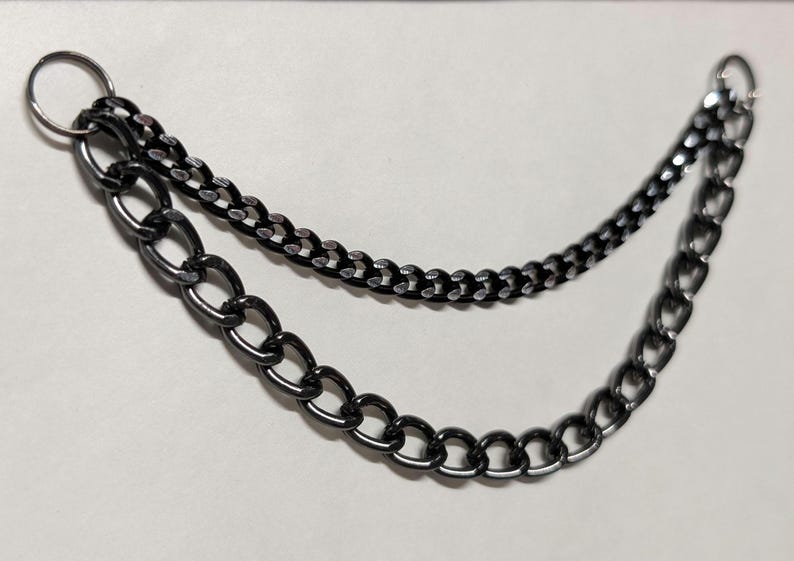 Peut inclure: Un accessoire de cha&icirc;ne &agrave; deux brins, de couleur m&eacute;tal de canon. La cha&icirc;ne sup&eacute;rieure est une cha&icirc;ne plus petite et plus d&eacute;licate, tandis que la cha&icirc;ne inf&eacute;rieure pr&eacute;sente des maillons plus grands et de forme ovale. Un anneau de couleur argent&eacute;e relie les cha&icirc;nes en haut.