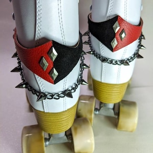 May include: White roller skates with black and red leather straps and silver studs. The straps have a diamond pattern. The skates have black chains with silver spikes.