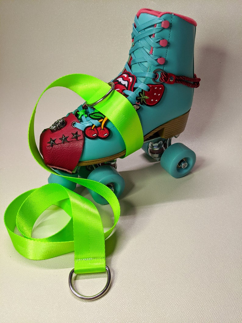 Puede incluir: Un par de patines de ruedas color turquesa con cerezas rojas, blancas y verdes y una fresa en el lateral. Los patines tienen una correa verde con un anillo plateado.