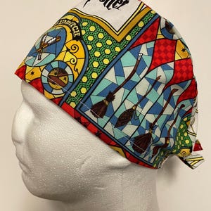 May include: A patterned surgical cap with a stained-glass effect, featuring brooms and the word "Potter". The cap is predominantly red, blue, yellow, and white. It is displayed on a mannequin head.