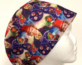 May include: A patterned scrub cap featuring a repeating design with images of a man in a red top hat and purple suit. The cap has a blue, purple, red, and yellow color scheme. The cap is on a white foam head.
