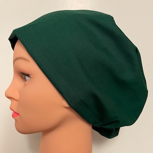 May include: A dark green scrub cap, designed to cover the head. The cap is made of a smooth fabric and has a simple, functional design. The cap is shown on a mannequin head.