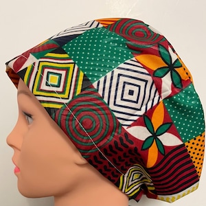 May include: A vibrant patchwork scrub cap with geometric and floral patterns in red, green, yellow, and white. The cap features squares, circles, and dotted designs. The cap is worn on a mannequin head.