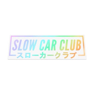 May include: A rectangular sticker with a holographic rainbow gradient. The text "SLOW CAR CLUB" is in large, bold, light blue and green letters. Below, smaller Japanese characters are also visible.