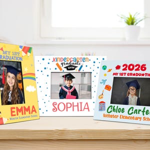 May include: Three graduation picture frames. The frames are yellow, white, and blue, each with a photo of a child in a graduation cap. The frames have the text "2026", "My 1st Graduation", and the names "Emma", "Sophia", and "Chloe Carter".