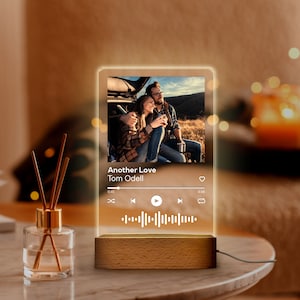 May include: A personalized night light featuring a photo of a couple, with the song title "Another Love" by Tom Odell displayed. The light has a wooden base and a clear acrylic panel.