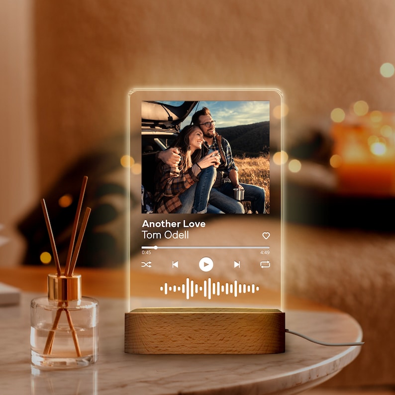 May include: A personalized night light featuring a photo of a couple, with the song title "Another Love" by Tom Odell displayed. The light has a wooden base and a clear acrylic panel.
