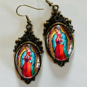 May include: A pair of bronze-coloured earrings with oval-shaped glass pendants featuring a colourful image of the Virgin Mary. The pendants have ornate metal frames.