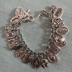 May include: A silver charm bracelet featuring various religious symbols and icons. The bracelet includes charms of crosses, saints, and other religious figures. The charms are attached to a silver chain, creating a detailed and meaningful piece of jewelry.