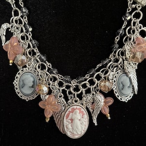 Puede incluir: Collar plateado con m&uacute;ltiples colgantes, incluyendo colgantes de camafeo, alas de &aacute;ngel y detalles de flores rosas. El collar presenta un dise&ntilde;o en capas con detalles de cuentas negras y metalister&iacute;a ornamentada, creando una est&eacute;tica vintage.