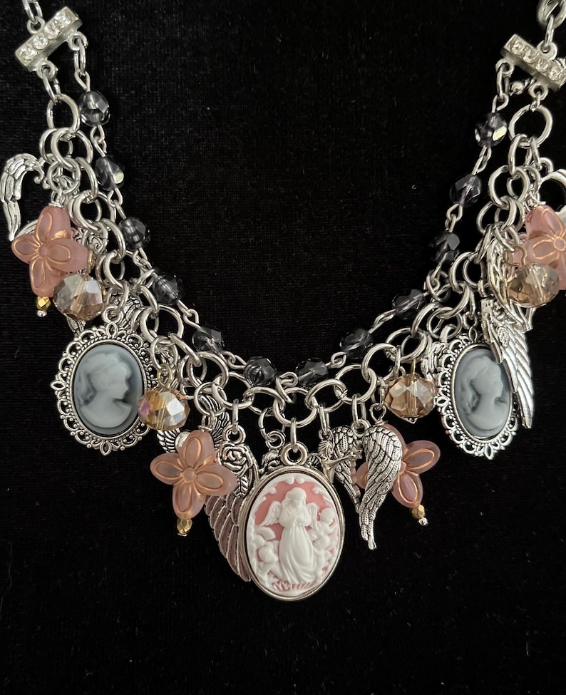 Puede incluir: Collar plateado con m&uacute;ltiples colgantes, incluyendo colgantes de camafeo, alas de &aacute;ngel y detalles de flores rosas. El collar presenta un dise&ntilde;o en capas con detalles de cuentas negras y metalister&iacute;a ornamentada, creando una est&eacute;tica vintage.
