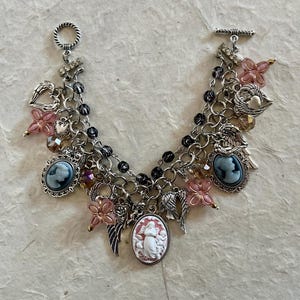 Puede incluir: Pulsera de abalorios plateada con colgantes de camafeo, cuentas de flores rosas, alas de &aacute;ngel y abalorios en forma de coraz&oacute;n. La pulsera tiene un cierre de palanca y una cadena con cuentas negras. Una joya &uacute;nica.