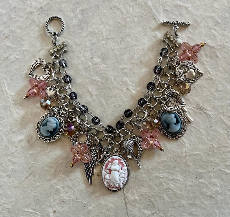 Puede incluir: Pulsera de abalorios plateada con colgantes de camafeo, cuentas de flores rosas, alas de &aacute;ngel y abalorios en forma de coraz&oacute;n. La pulsera tiene un cierre de palanca y una cadena con cuentas negras. Una joya &uacute;nica.