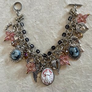 Puede incluir: Pulsera de plata con m&uacute;ltiples colgantes. La pulsera presenta colgantes de camafeo, dijes de flores rosas, dijes de alas de &aacute;ngel y dijes de coraz&oacute;n. La pulsera tiene un cierre de palanca y est&aacute; hecha de metal plateado y cuentas negras.