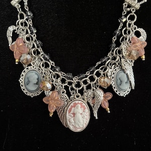 Puede incluir: Una pulsera de dijes plateada con m&uacute;ltiples cadenas y un cierre de palanca. La pulsera presenta colgantes de camafeo, dijes de alas de &aacute;ngel y detalles de flores rosas. Los dijes adicionales incluyen cuentas facetadas y peque&ntilde;as cuentas doradas. El fondo es negro.