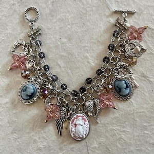 Puede incluir: Pulsera de abalorios plateada con colgantes de camafeo, alas de &aacute;ngel, cuentas de flores rosas y abalorios en forma de coraz&oacute;n. La pulsera tiene un cierre de palanca y m&uacute;ltiples hilos de cadena con cuentas negras.
