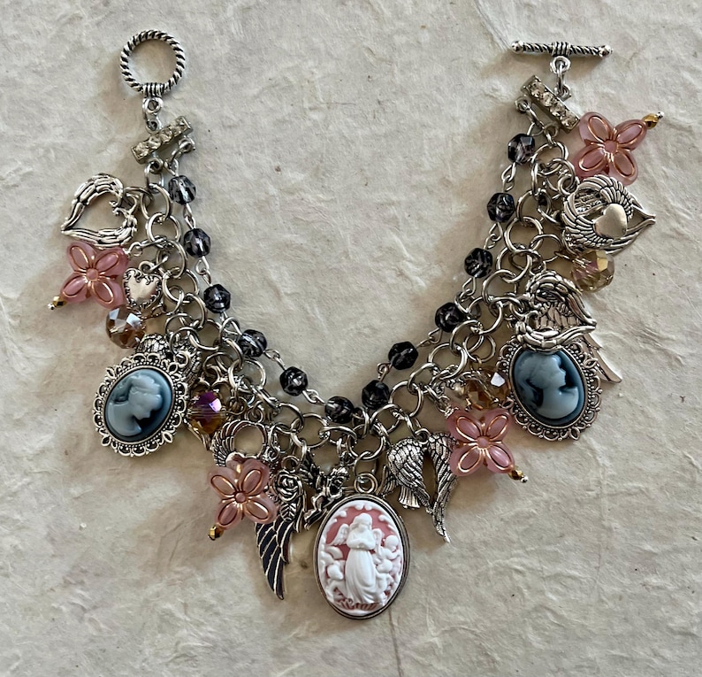 Puede incluir: Pulsera de abalorios plateada con colgantes de camafeo, alas de &aacute;ngel, cuentas de flores rosas y abalorios en forma de coraz&oacute;n. La pulsera tiene un cierre de palanca y m&uacute;ltiples hilos de cadena con cuentas negras.