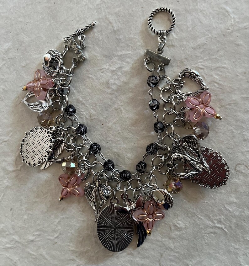 Puede incluir: Pulsera de abalorios plateada con cierre de palanca. La pulsera presenta m&uacute;ltiples cadenas y una variedad de abalorios, que incluyen cuentas de flores rosas, hojas plateadas y abalorios redondos y ovalados decorativos. Las cuentas negras se intercalan a lo largo de las cadenas.
