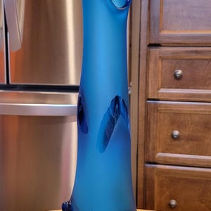 May include: A tall, vibrant blue glass vase with a unique, organic shape. The vase has a flared top and decorative, dark blue accents. It stands approximately 15 inches tall, perfect for displaying flowers or as a decorative piece.