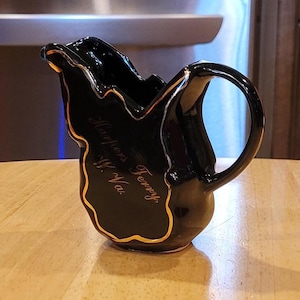May include: Black ceramic creamer in the shape of the state of Virginia with gold trim and the words "Virginia is for Lovers" written on the side.