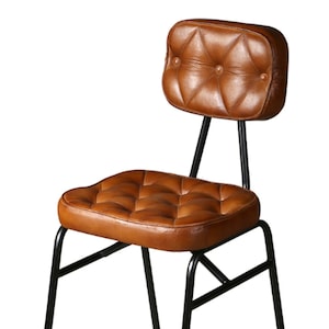 Puede incluir: Una silla de cuero marrón con respaldo y asiento capitoné. La silla tiene un marco y patas de metal negro.