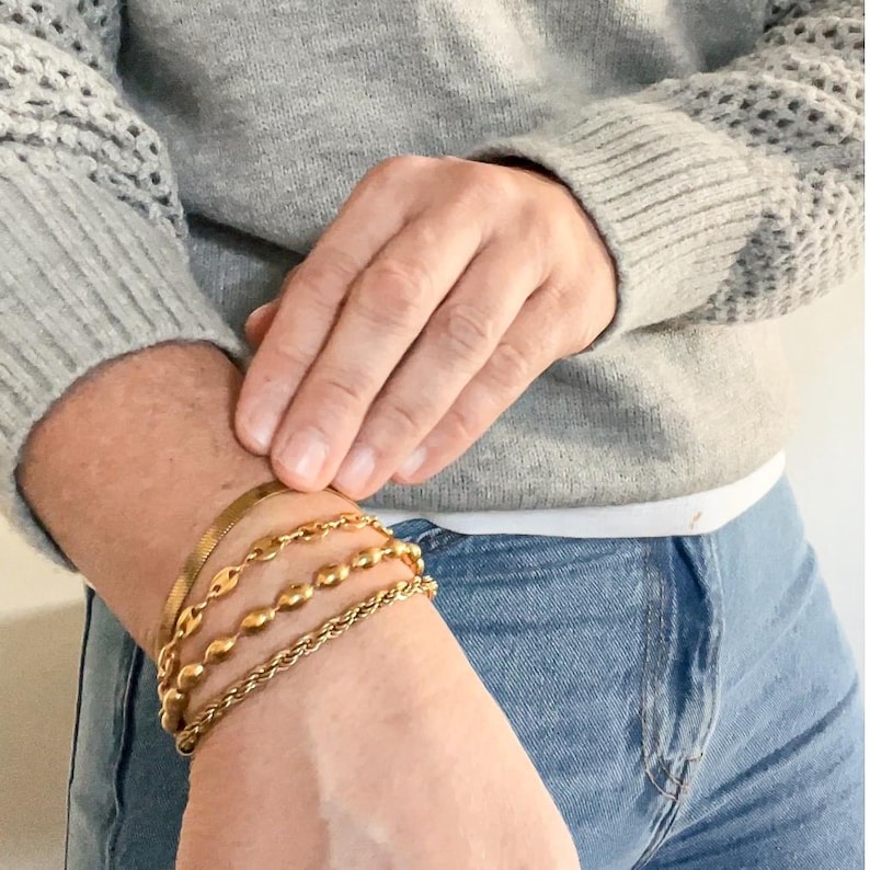 Puede incluir: Una persona lleva un su&eacute;ter gris y jeans azules con cuatro pulseras doradas en la mu&ntilde;eca.