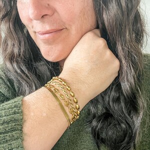 Puede incluir: Una mu&ntilde;eca de mujer con cuatro pulseras de oro. Las pulseras est&aacute;n apiladas una encima de la otra y est&aacute;n hechas de diferentes estilos de cadenas.