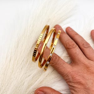 May include: Three gold bangles, one with a textured surface and two with clear stones.