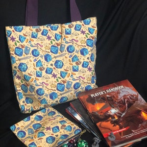 May include: A yellow tote bag and a matching zippered pouch with a blue and white dice pattern. The tote bag has purple handles. The pouch is filled with blue and white dice. A stack of books with the title "Dungeons & Dragons Player's Handbook" is in the background.